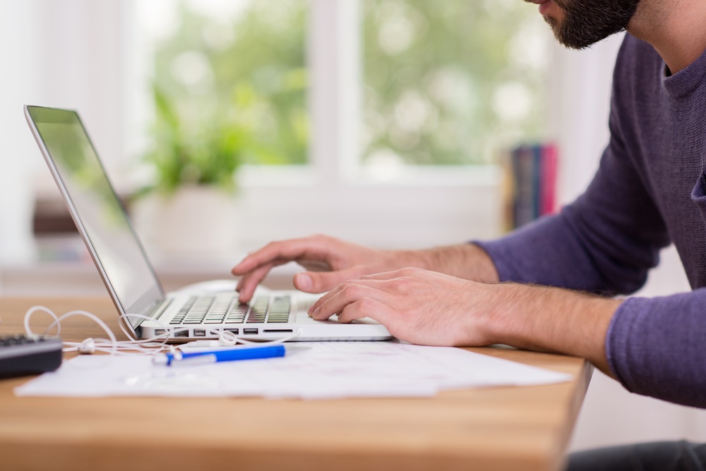 Close up low angle view of a man working from home on a laptop computer sitting at a desk surfing the internet.jpeg