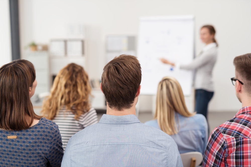 Rear View of Young Office Workers in Casual Outfits Listening to a Top Manager Explaining Something Using Illustrations..jpeg